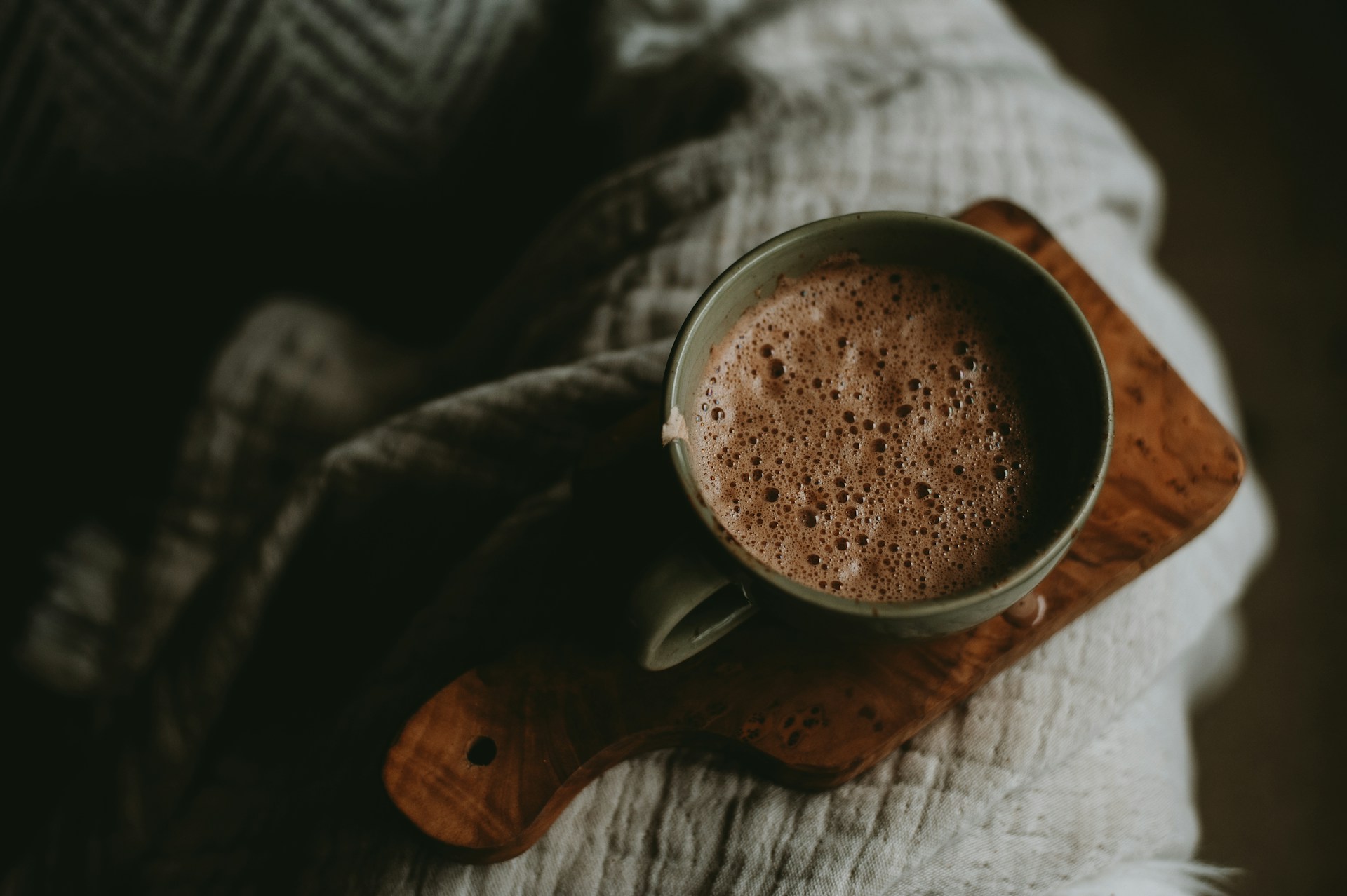Mug of hot chocolate resting on the arm of a sofa.
