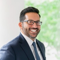 Corporate head and shoulders shot of a smiling man with a beard and glasses.