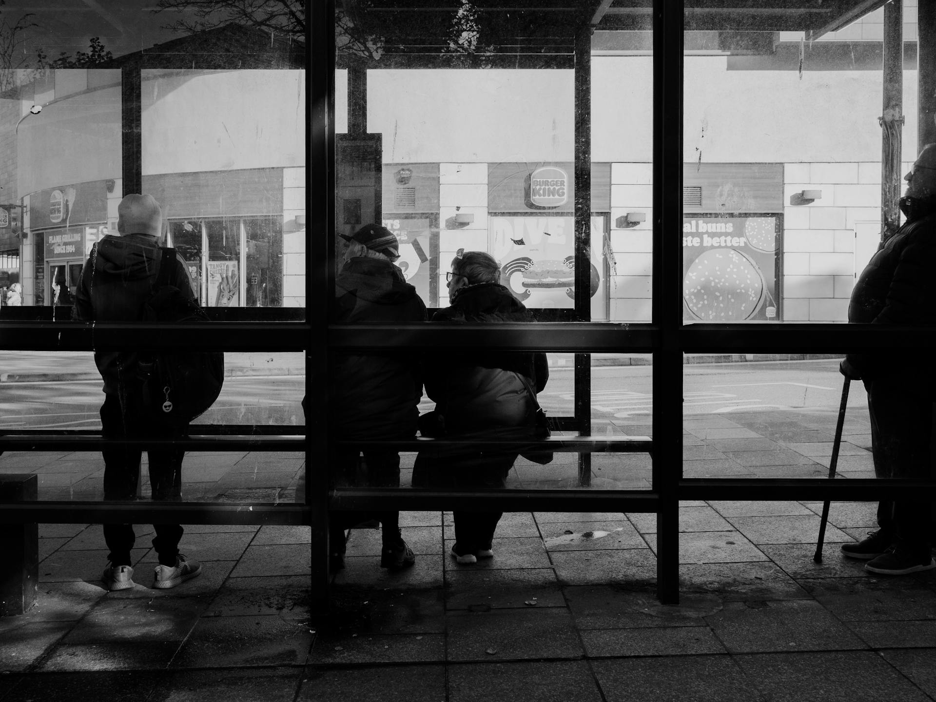 Photo of people sitting in  a dark bus shelter. Image by Lisa from Pexels on pexels.com