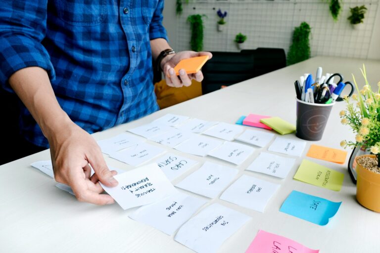 Person (only their arms and torso can be seen) in a checked shirt arranging post it notes and cue cards in lines on a desk.