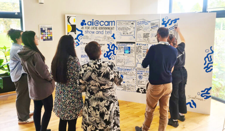 Group of people standing in front of a large banner full of illustrations and words around ai@cam: AI for local government