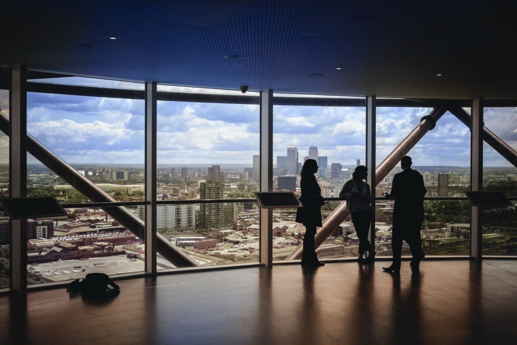View of a cityscape from a skyscraper viewing room with large windows. Photo by Charles Forerunner via Unsplash